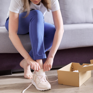 Femme mettant des baskets roses, assise sur un canap&eacute; avec bo&icirc;te &agrave; chaussures.